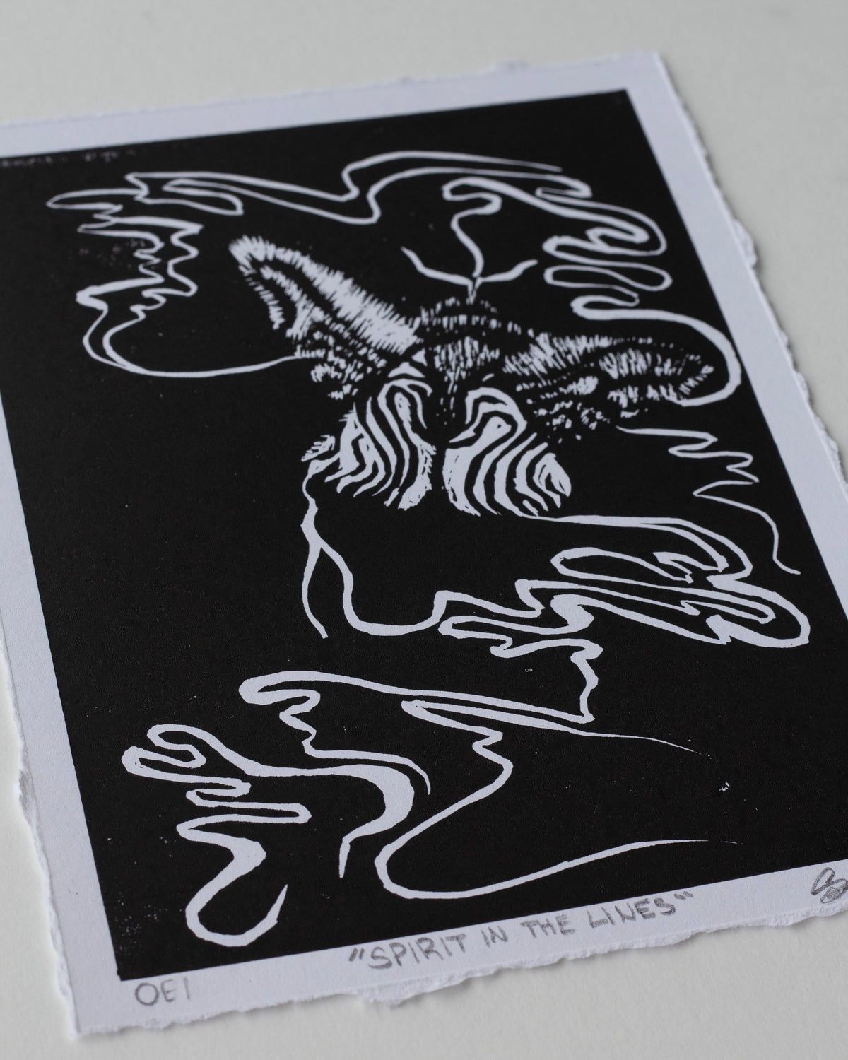A black and white art print featuring an abstract, stylized moth with flowing line art, photographed on a light neutral background.