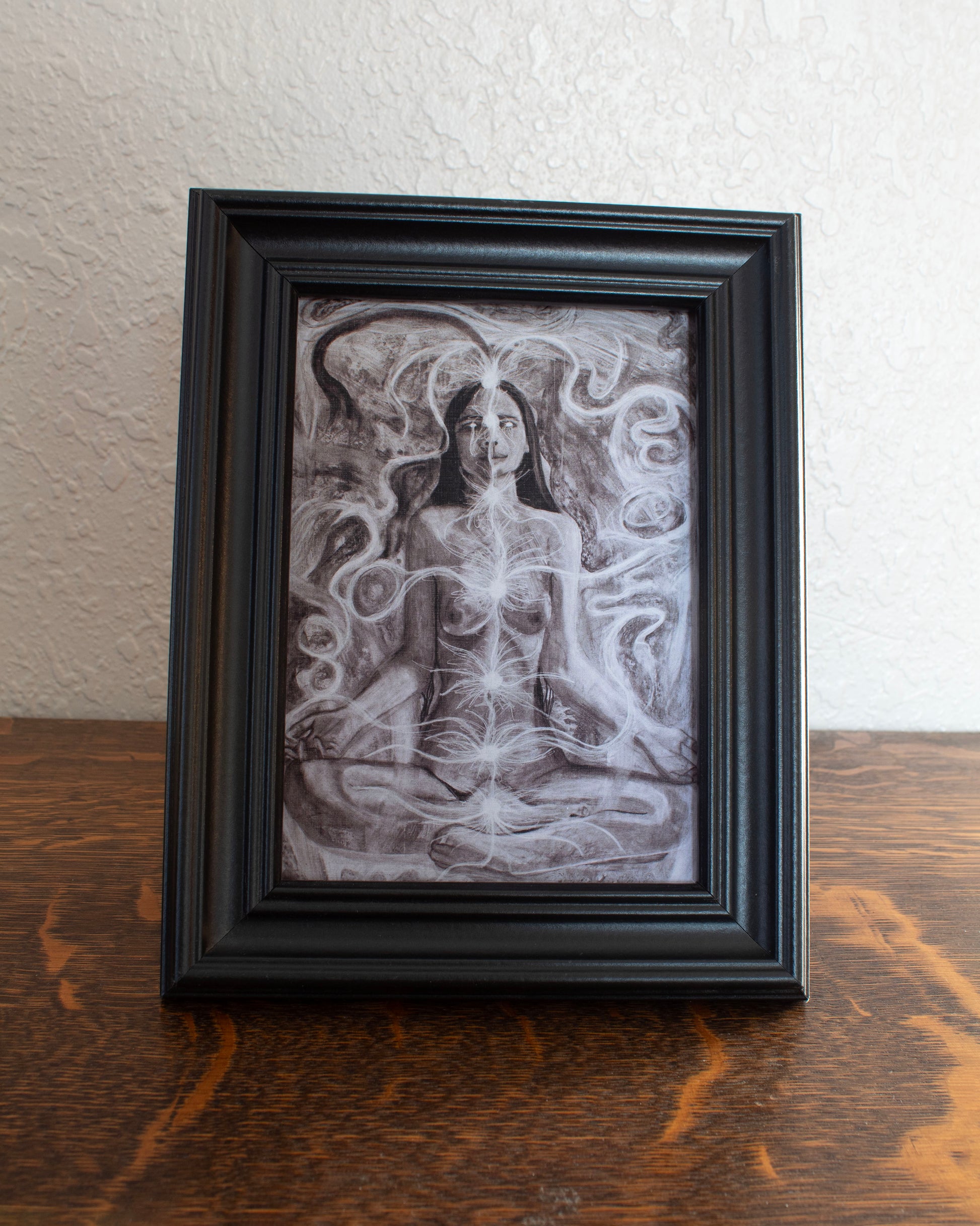 Artistic depiction of a nude figure with intricate patterns and energy lines flowing around and into the 7 chakra points. Framed artwork of a nude figure with abstract patterns on a wooden surface.