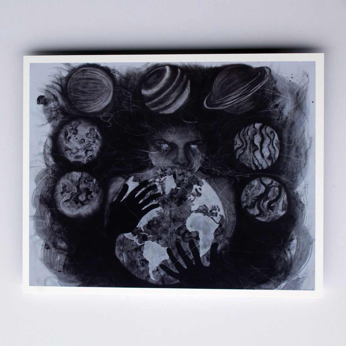 A monochrome artwork depicting a figures face and hands holding a globe, surrounded by stylized planets and abstract circular forms in black, gray, and white.